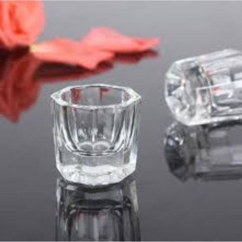 Clear glass dappen dish with faceted sides, a round opening and a thick base, with a second dish lying beside it.