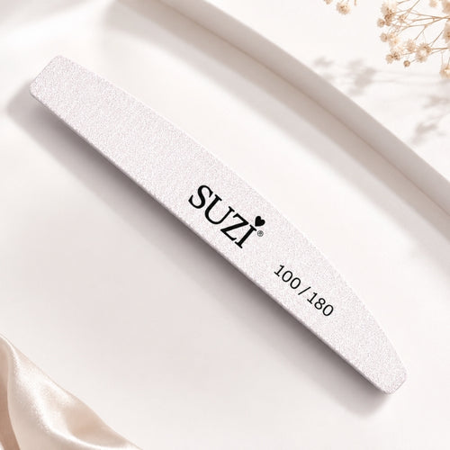 A white nail file with a textured, glittery finish and the brand name 'SUZI' printed in black, shown on a clean white background with decorative dried flowers and satin fabric.